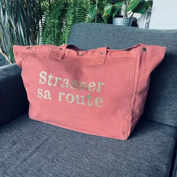 Sac fourre-tout vieux rose avec slogan "Strasser sa route" en doré pailleté.