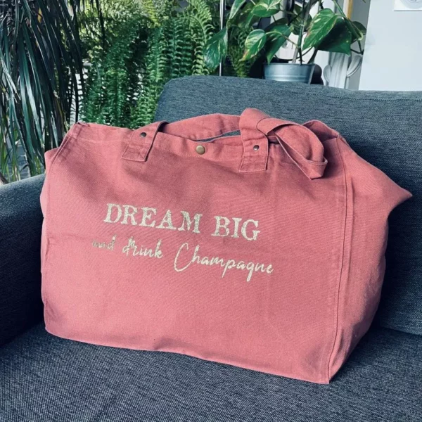 Sac fourre-tout vieux rose avec slogan "Dream Big and drink Champagne" en doré pailleté.