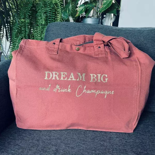 Sac fourre-tout vieux rose avec slogan "Dream Big and drink Champagne" en doré pailleté.