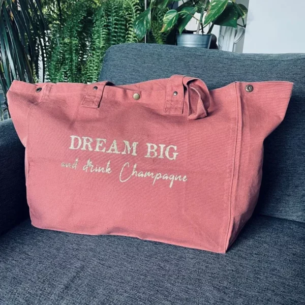 Sac fourre-tout vieux rose avec slogan "Dream Big and drink Champagne" en doré pailleté.