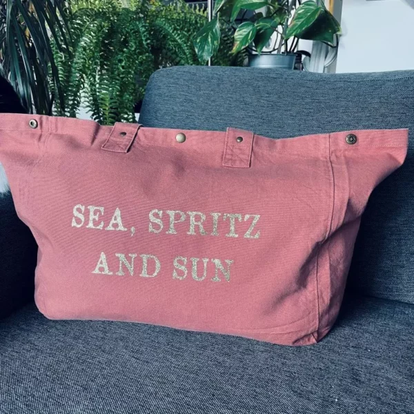 Sac fourre-tout vieux rose avec slogan "Sea, Spritz and Sun" en or pailleté.